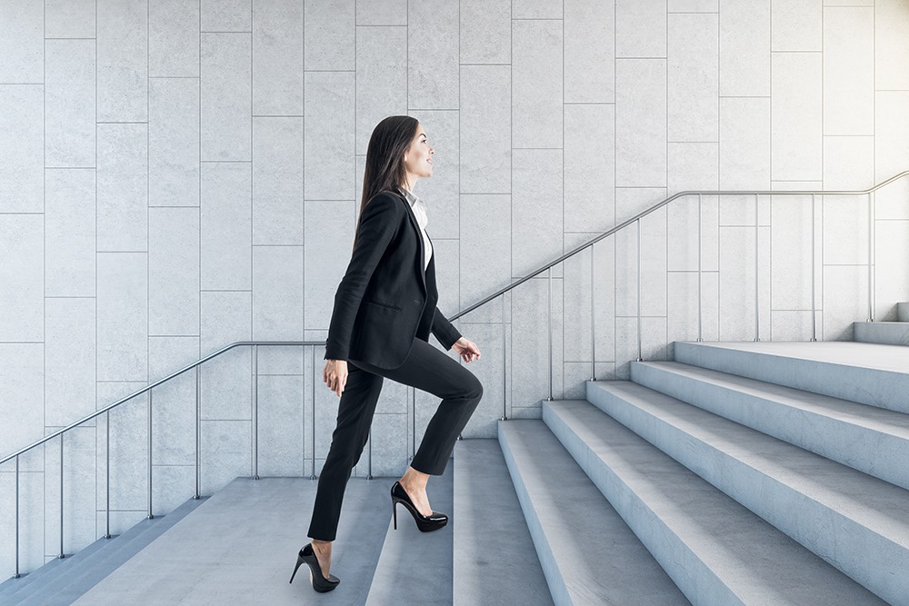 A slim woman wearing a business suit is going up the stairs